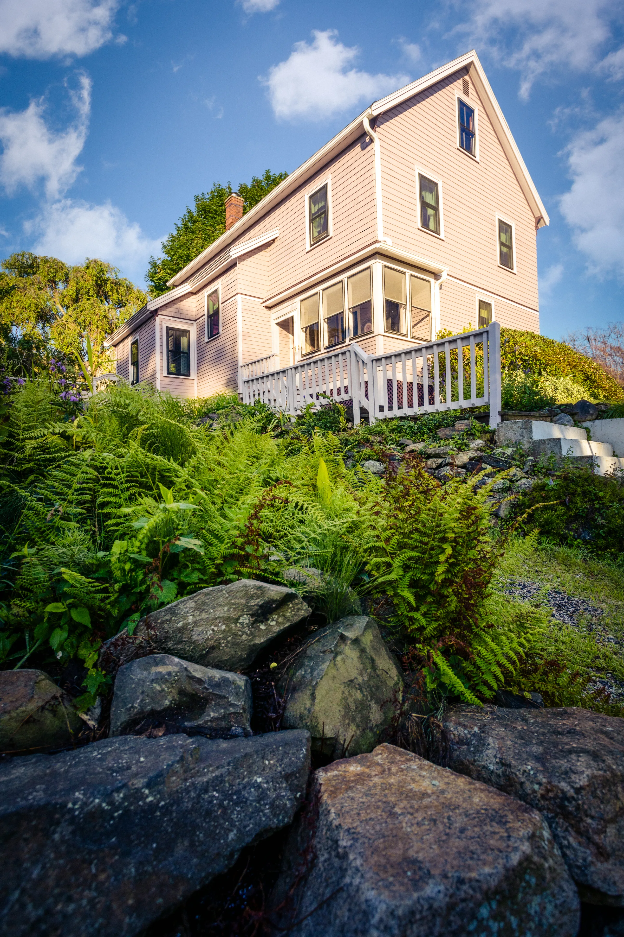 Mauve-painted side elevation above a fern-filled rock garden and white railing