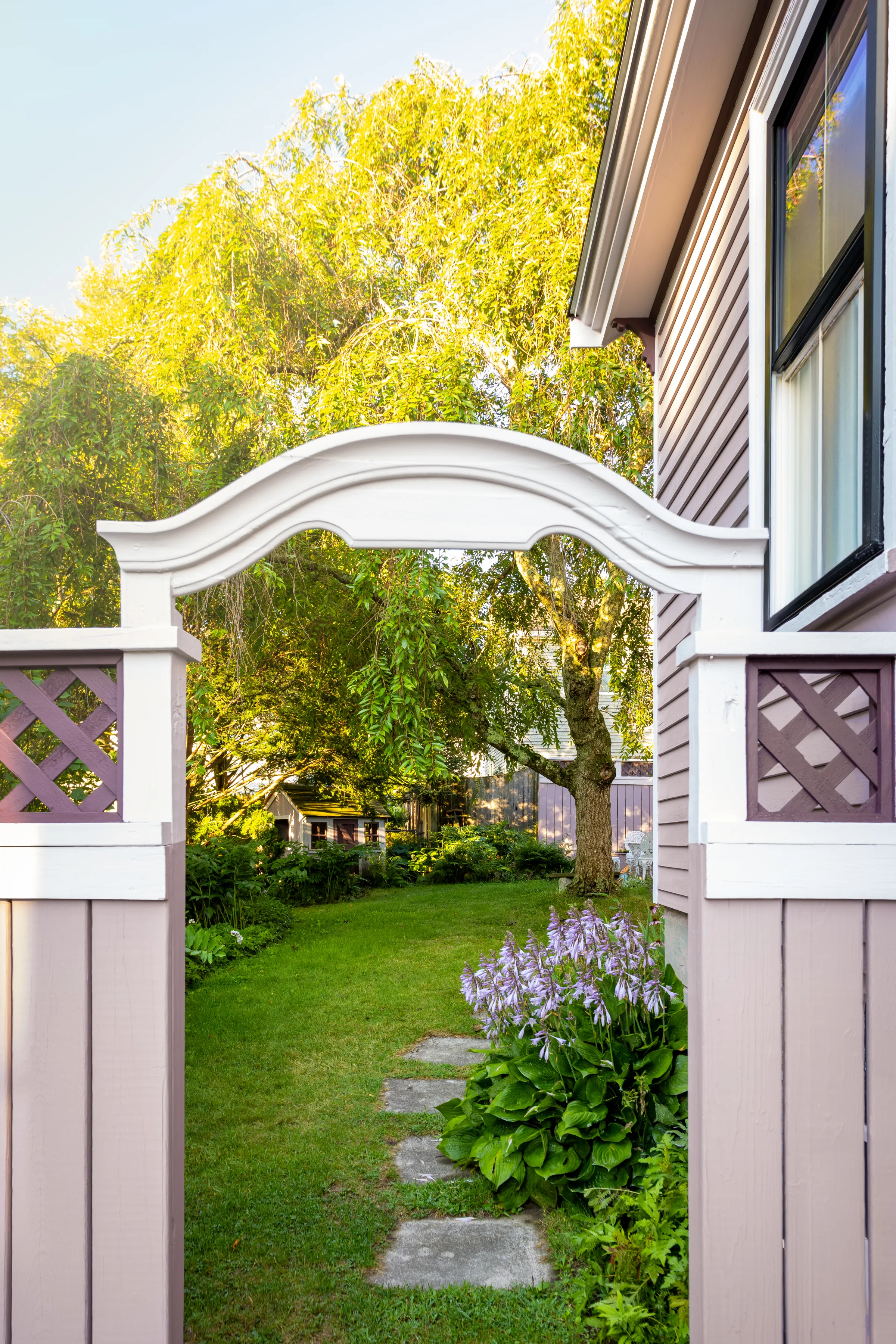 Curved garden gate with light trim, purple lattice panels, and mauve vertical boards