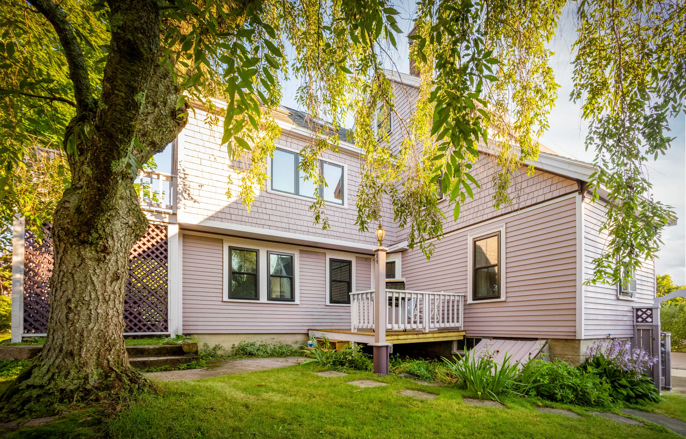 Garden-side exterior with mauve siding, light trim, purple lattice, and a small deck
