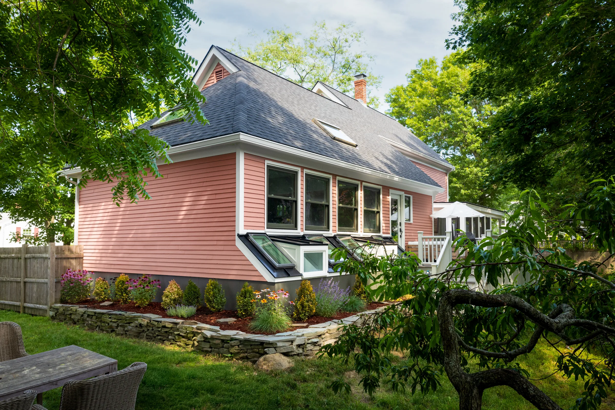 Rear garden view with coral siding, dark foundation, white trim, and basement windows
