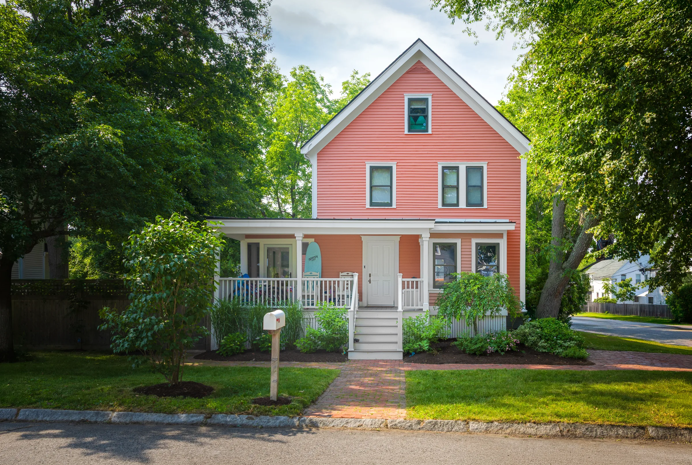 Wide front view of a coral historic home framed by mature trees