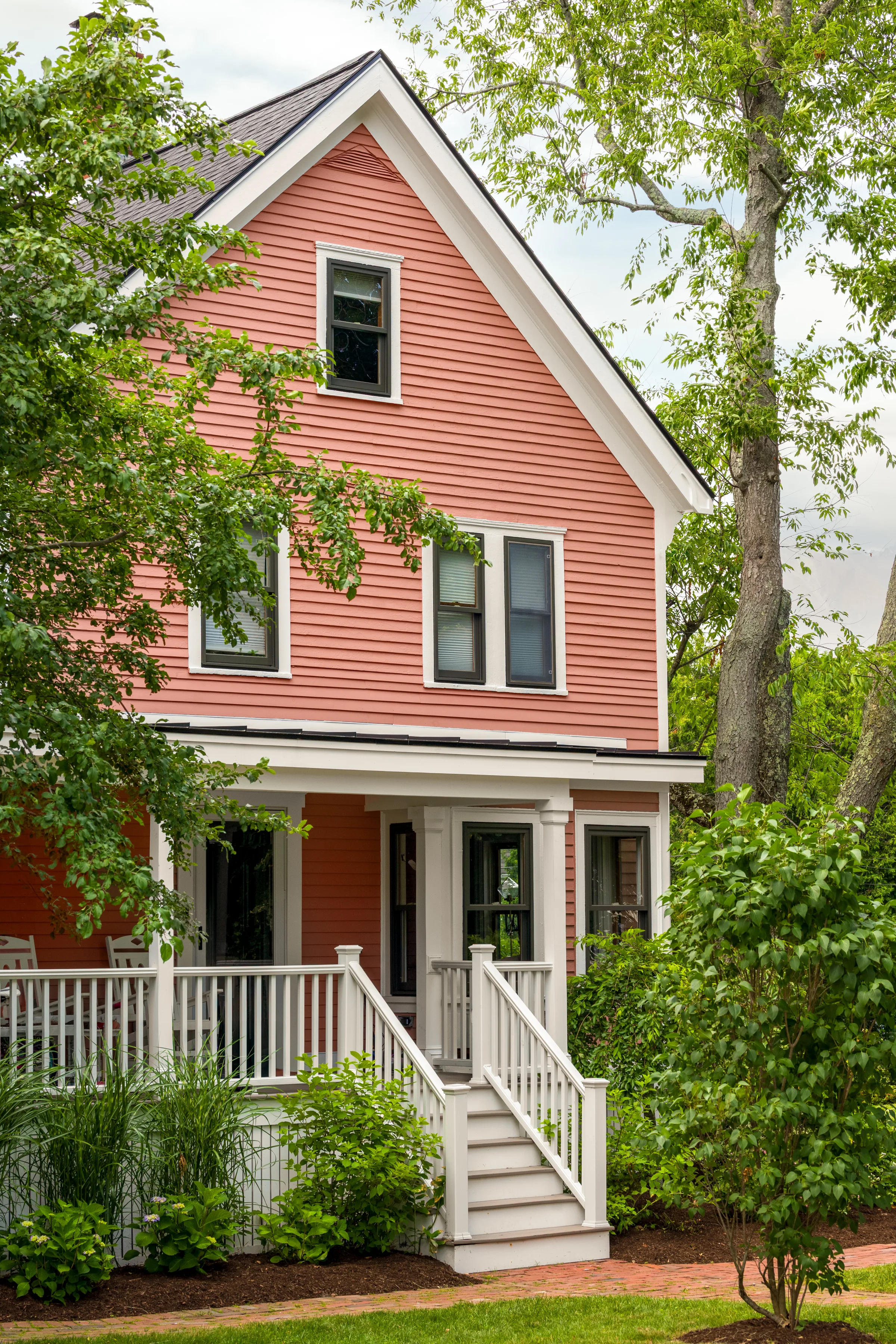 Angled front view showing coral siding, white porch railings, and dark windows