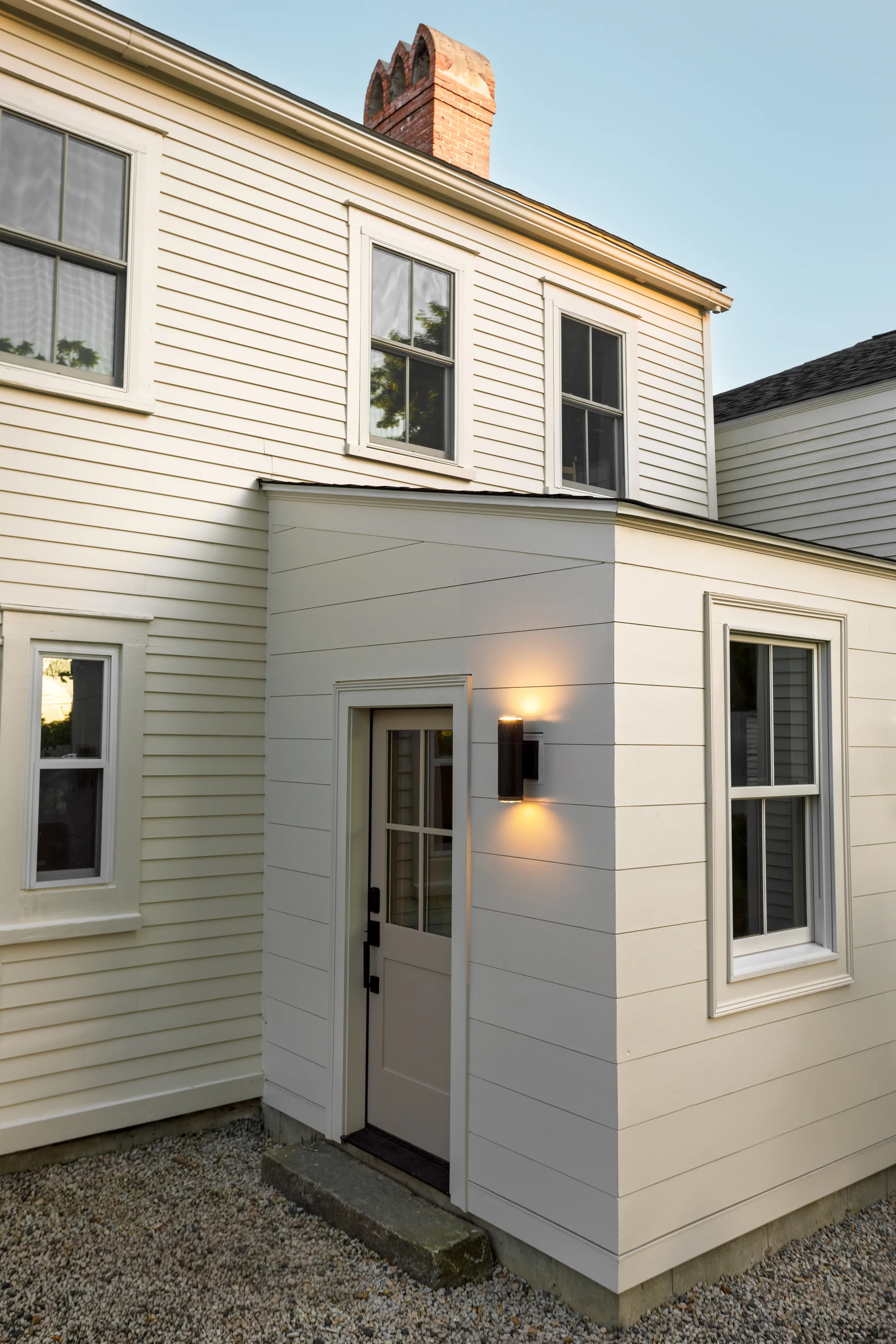 Light-painted siding and trim around a small rear entry with tall windows