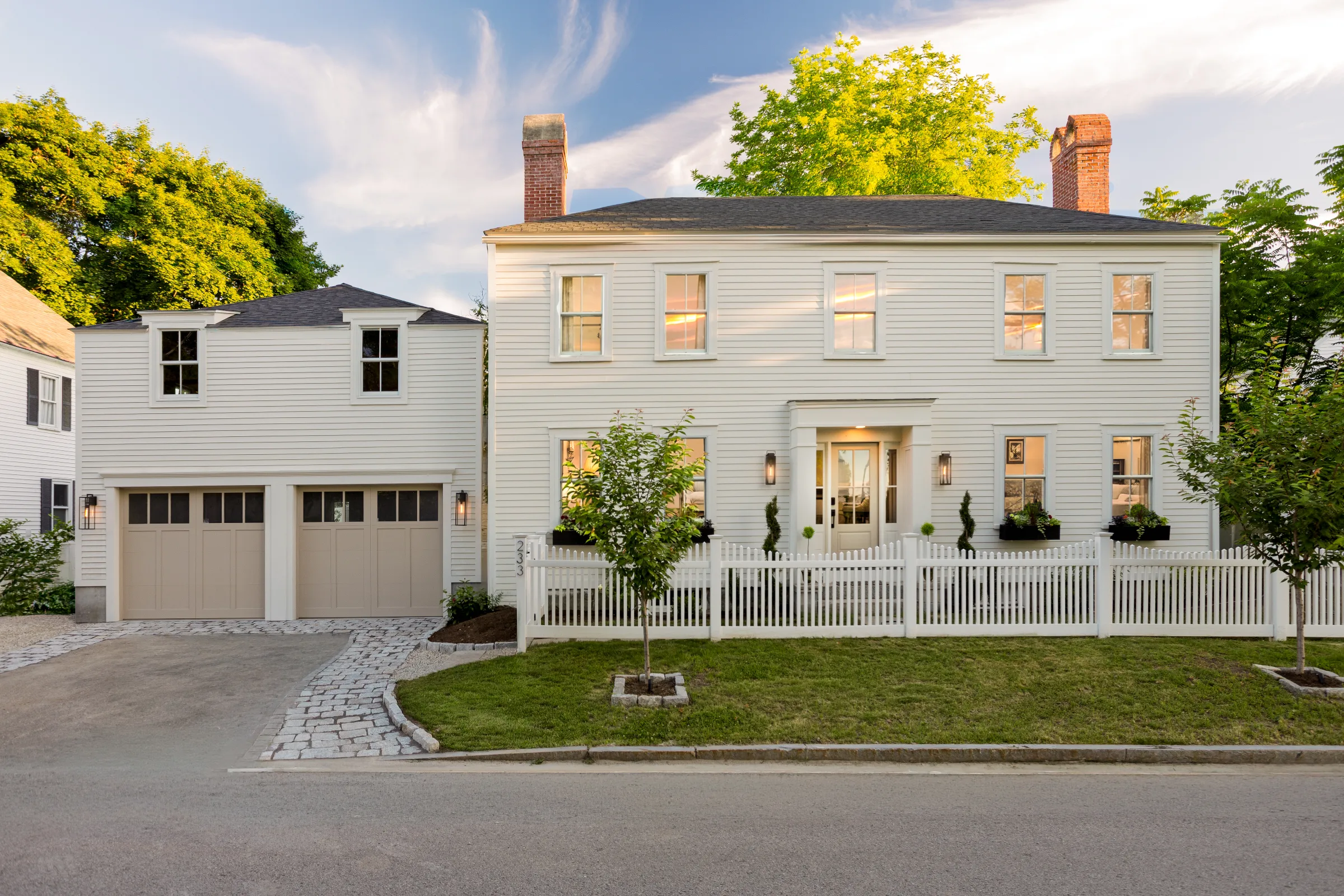 Front view of a light-painted two-story home with a two-door garage and white fence