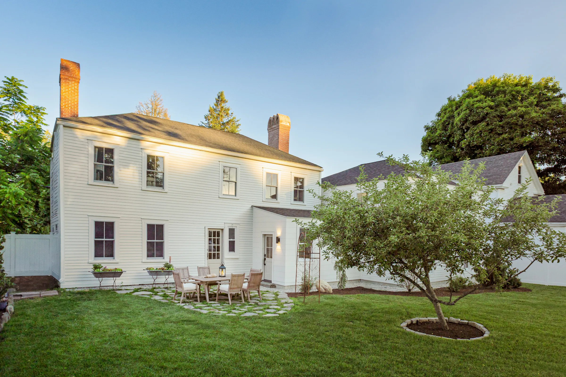Rear elevation of a light-painted historic home overlooking a lawn and patio