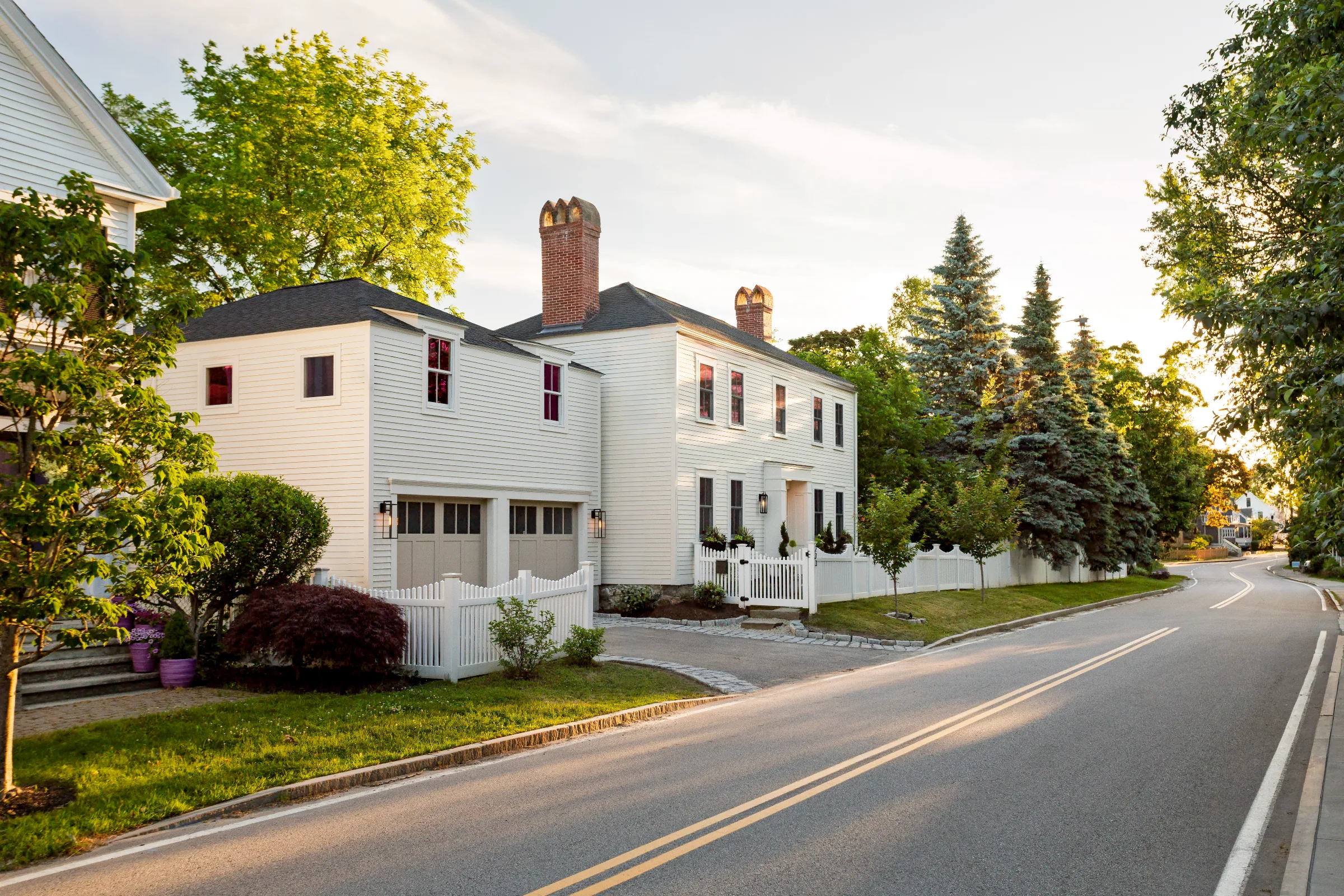 Wide street view of a light-painted historic home with an attached two-door garage
