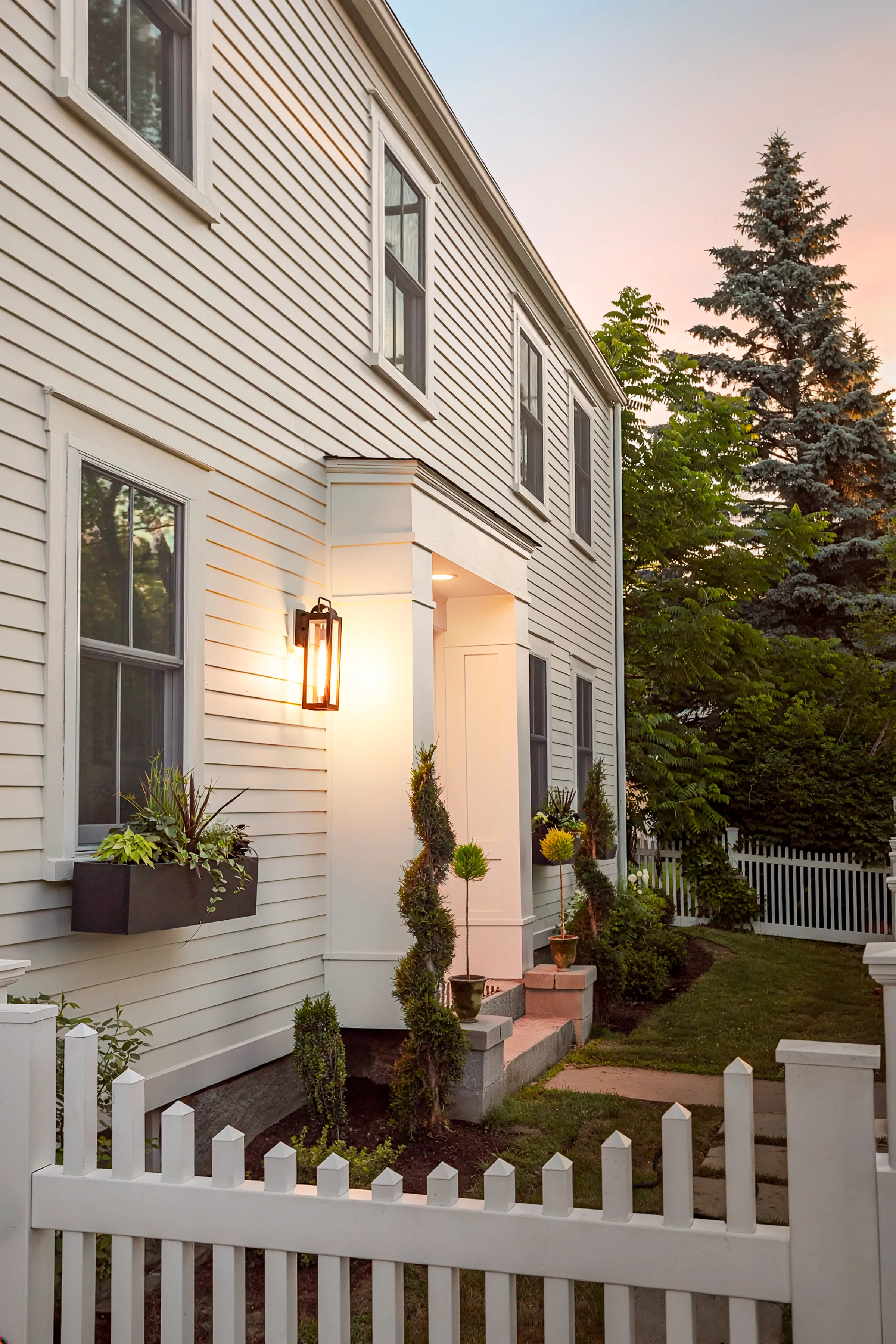 Light-painted front entry, clapboard siding, window trim, and white picket fence